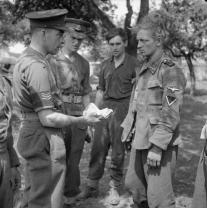 A British Military Policeman questions a German POW found with a large amount of Russian banknotes on 6 June 1944. (IWM B7897)